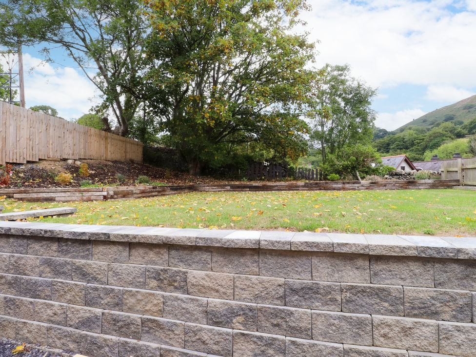 A garden with a stone wall and trees at 95 Cae America in Llanfairfechan