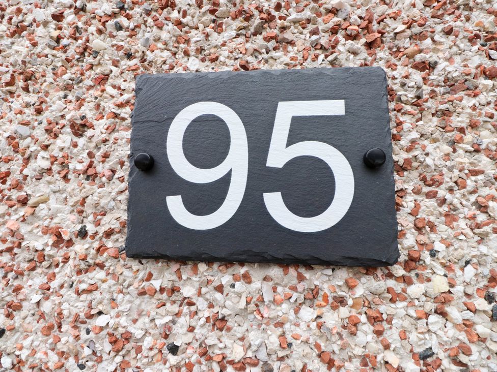 A house number 95 on a slate plaque attached to a textured wall at 95 Cae America Llanfairfechan