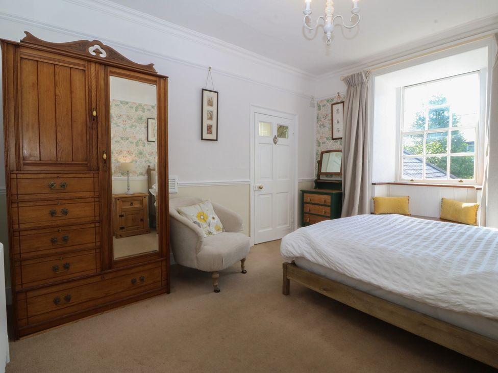 A bedroom with a wardrobe, bed, and armchair at Tan y Gader in Dolgellau