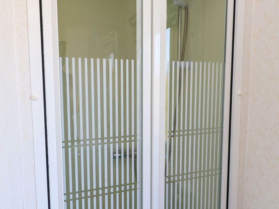 A shower with a glass door and shower head at The Lodge in Amlwch