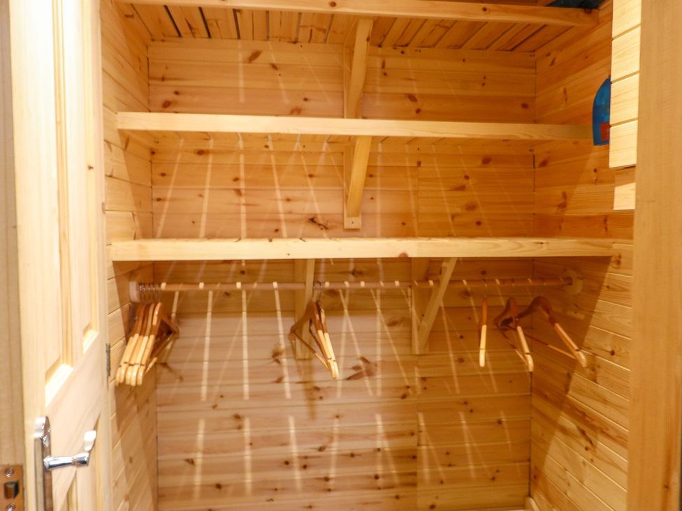 A closet with wooden shelves and coat hangers at The Cabin in Amlwch