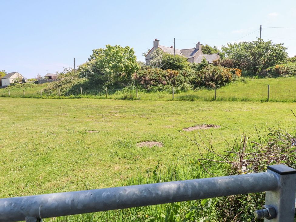 An outdoor area with grass and trees and houses in the background at The Cabin in Amlwch