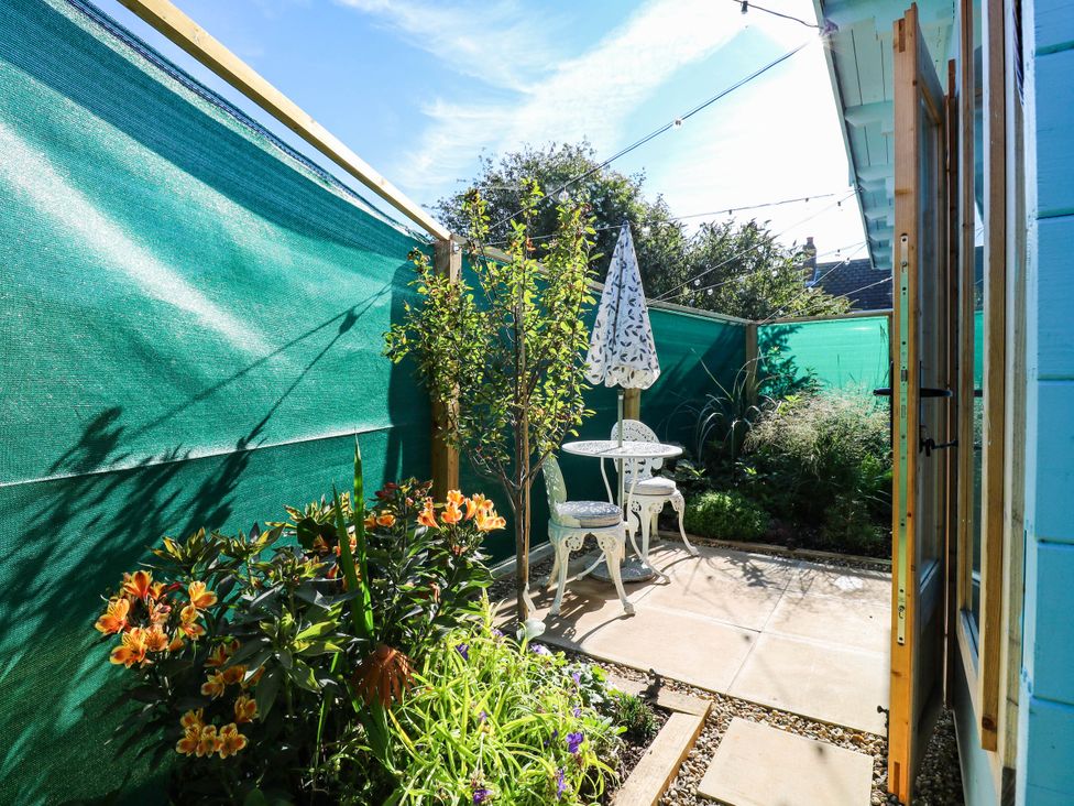 A garden with a table and chairs beside flowers at The Cabin in Herne Bay