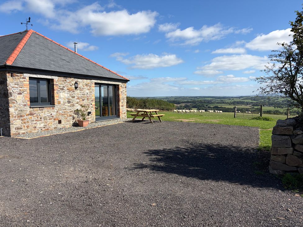 An exterior view of a house with a picnic table and sheep in a field at High View Barn in Launceston