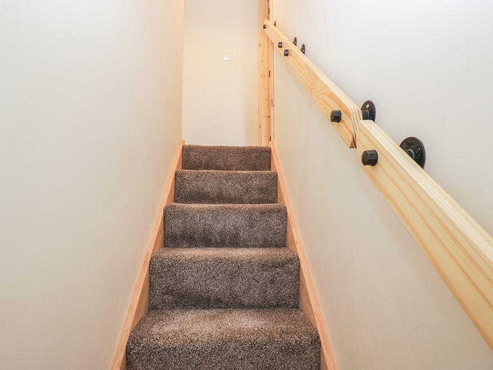A staircase with carpet and a wooden handrail at Bluebell Cottage in Heysham