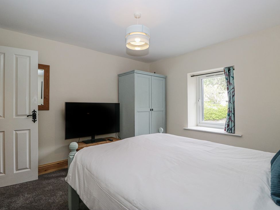 A bedroom with a bed, television, wardrobe, and window at Bluebell Cottage in Heysham