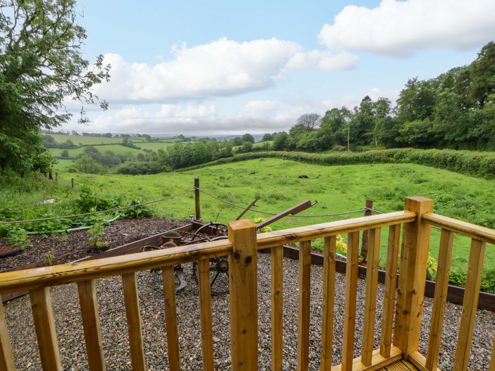 An outdoor view of a grassy field with trees and a wooden deck at The Hut in Llandysul