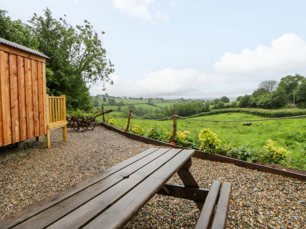An outdoor scene with a wooden cabin and bench overlooking a landscape at The Hut in Llandysul