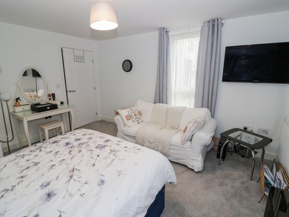 A bedroom with a bed, mirrored dresser, sofa, and television at 4 Goldcrest Close in Daventry