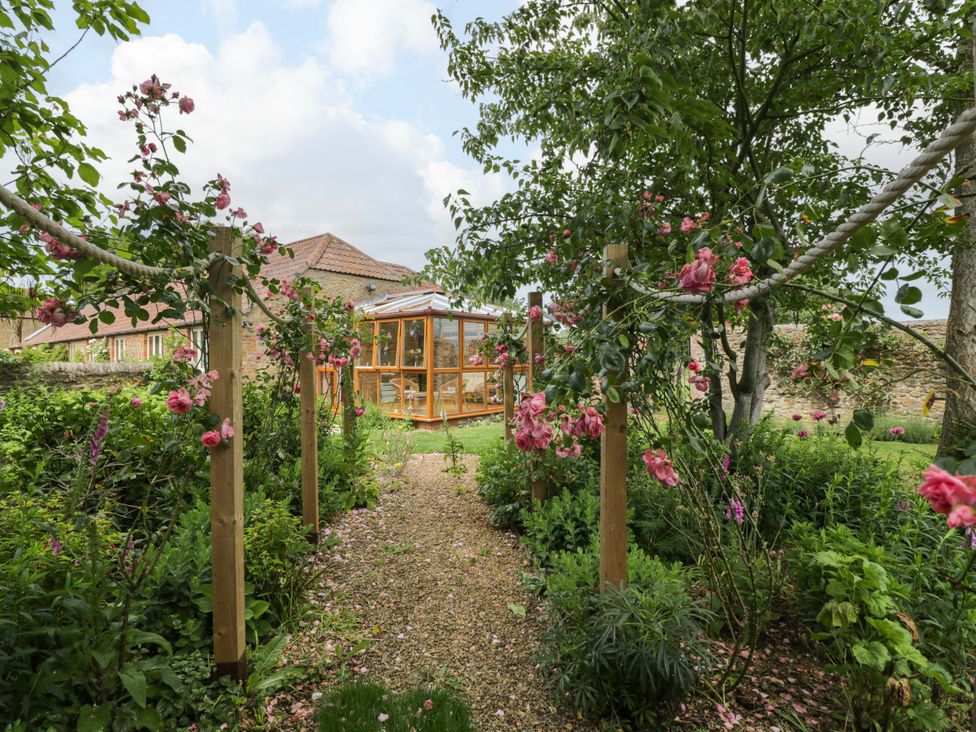 A garden with a pathway and flowers leading to a greenhouse at The Garden Studio in Bremhill near Calne