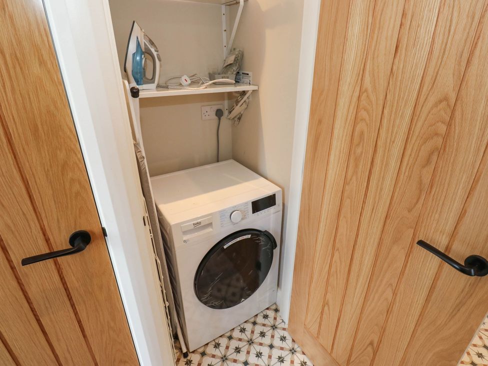 A laundry room with a washer and iron on a shelf at The Stables in Stainland