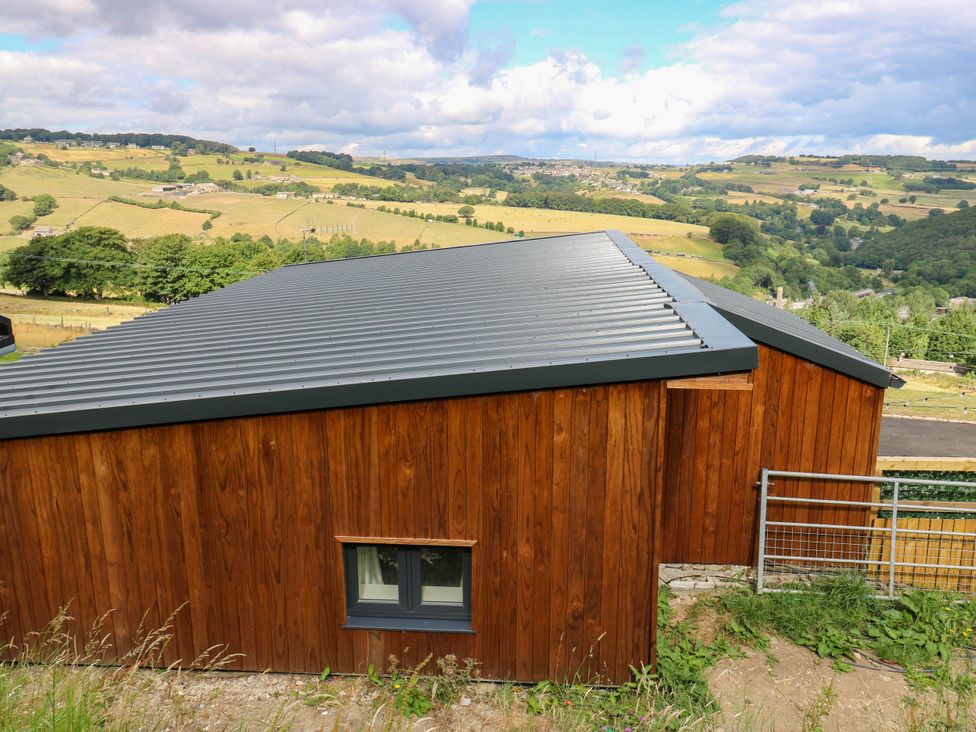 A wooden building with a metal roof on a hillside at The Stables in Stainland