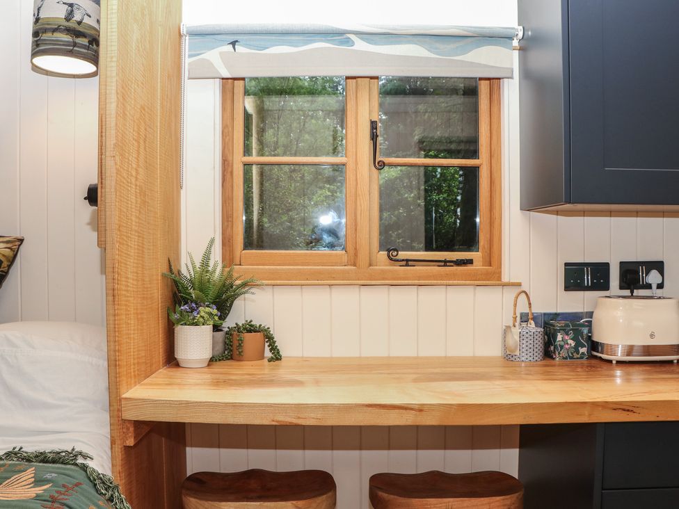 A kitchen with a wooden table and stools at Ridden Brake shepherds hut in Yelverton