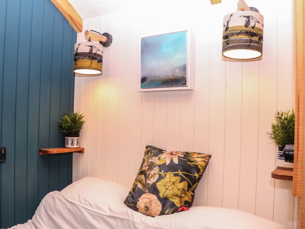 A bedroom with a bed, pillow, plant, light fixture and wall art at Ridden Brake shepherds hut Yelverton