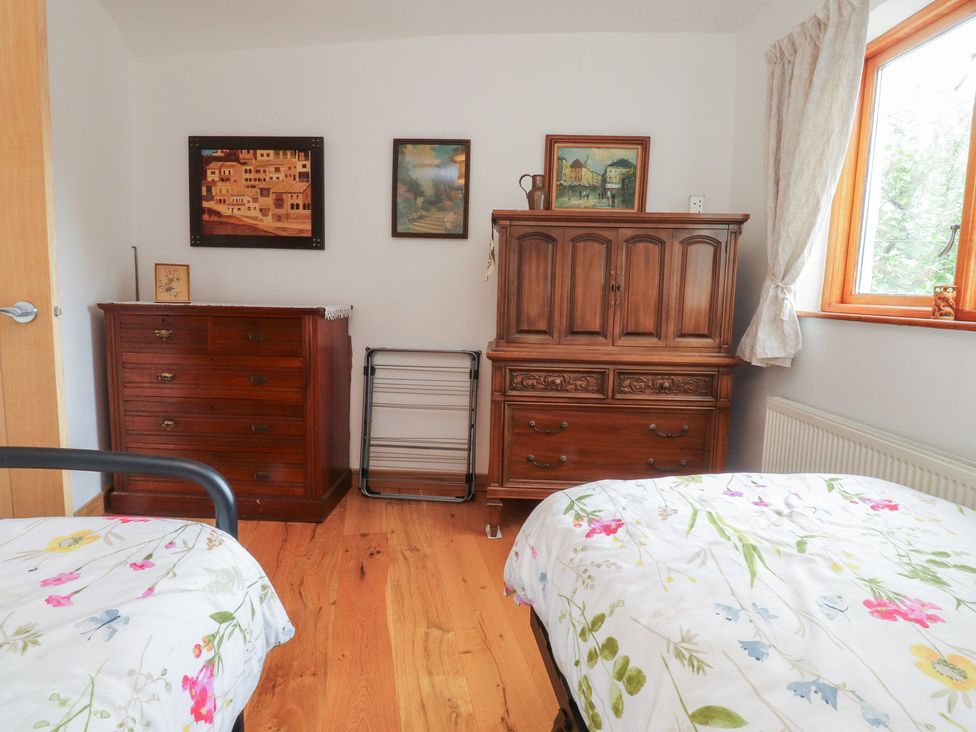A bedroom with a dresser, chest of drawers, and paintings at The Cottage in Giggleswick