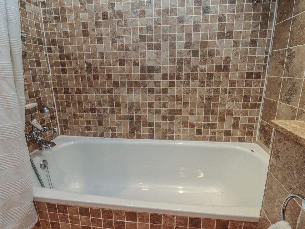 A bathroom with a bath tub and tiled walls at The Cottage in Giggleswick