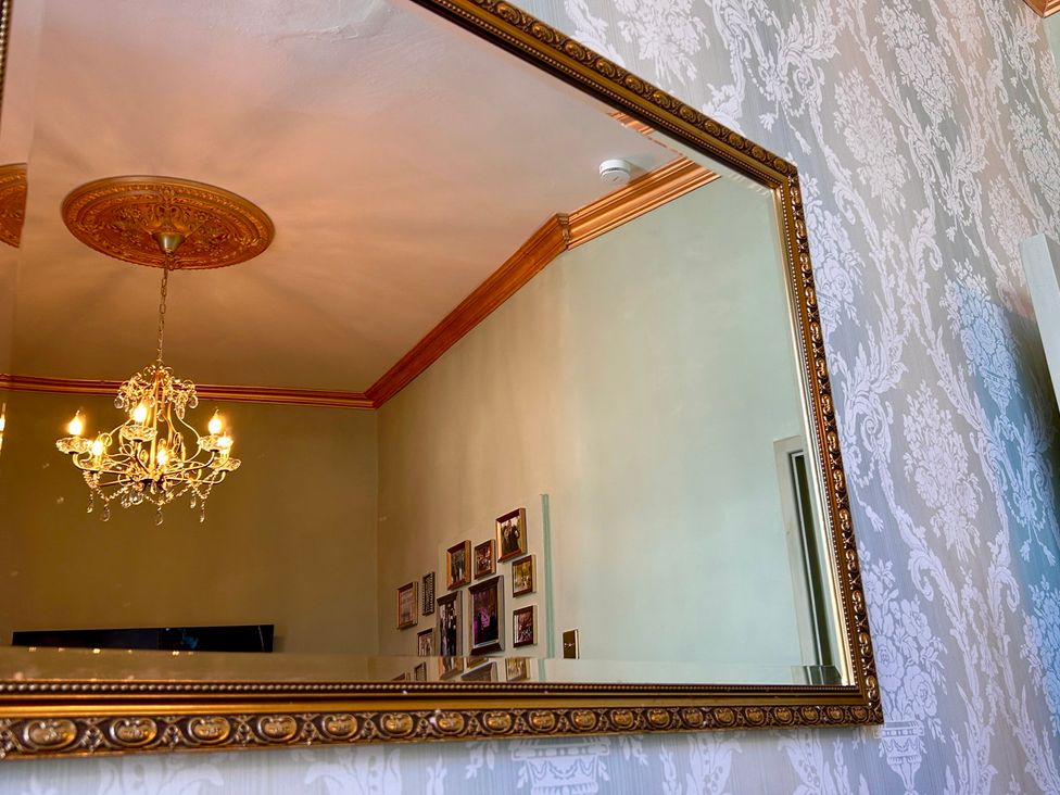 A mirror reflecting a chandelier and wall photos at Downton I in Alnwick