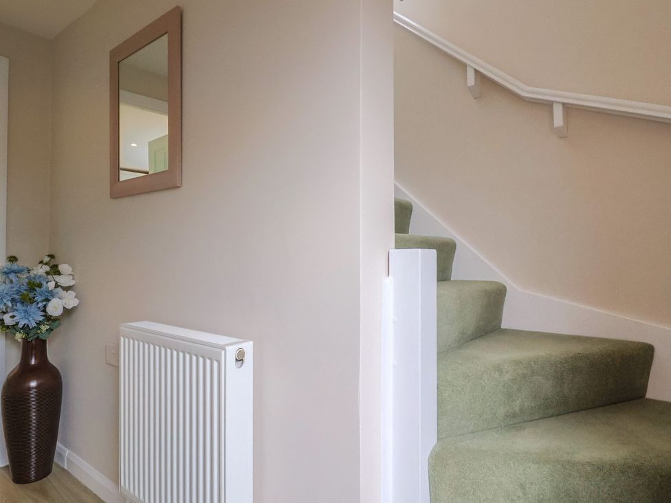 A hallway with a staircase and a vase of flowers at Frome View Wool