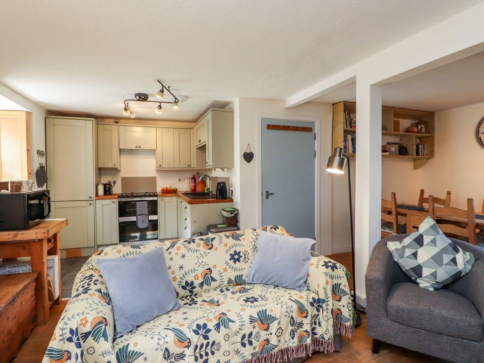 A living room with a sofa and kitchen area at Scoops’ Nook in Caernarfon