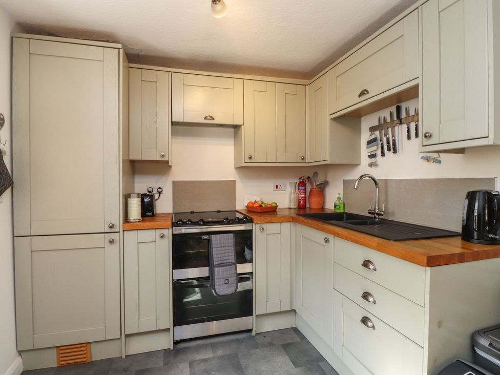 A kitchen with cabinets, stove, sink, and kettle at Scoops’ Nook, Caernarfon