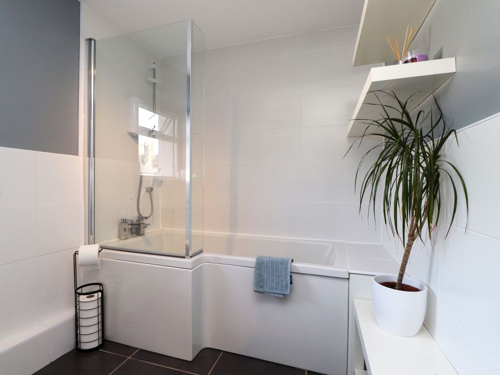 A bathroom with a bathtub, shower screen and plant at Scoops’ Nook Caernarfon