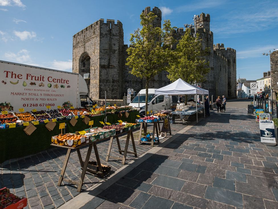 An outdoor market with fruit stalls and a castle in the background at Scoops’ Nook, Caernarfon