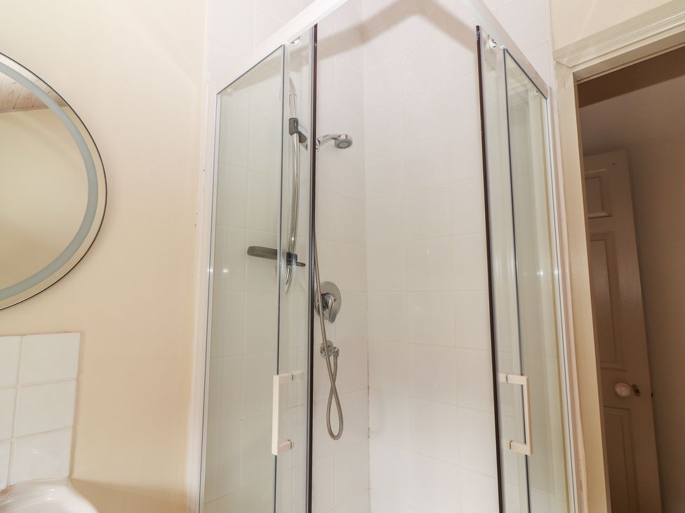 A shower enclosure with a mirror and tiles at The Coach House Cottage BALLYCOMMON