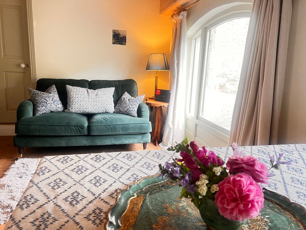 A living room with a green sofa and flowers on a table at The Coach House Cottage Ballycommon