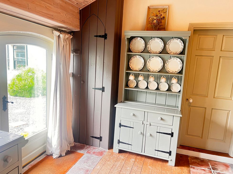 A kitchen with a cabinet displaying plates and a window at The Coach House Cottage in Ballycommon