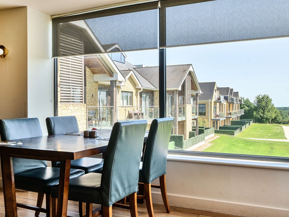 A dining room with a table and chairs overlooking buildings and grass at Cotswolds Apartments 4B/S8 in Chipping Norton