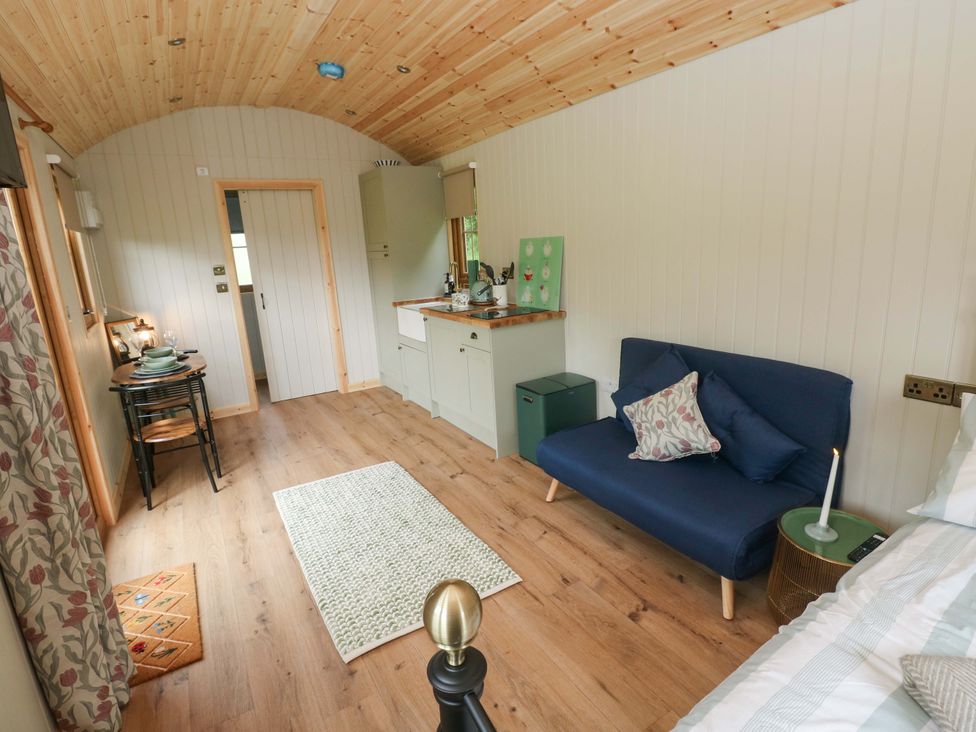 A living room with a sofa, table, and kitchenette at Shepherd Hut 1 in Llandeilo