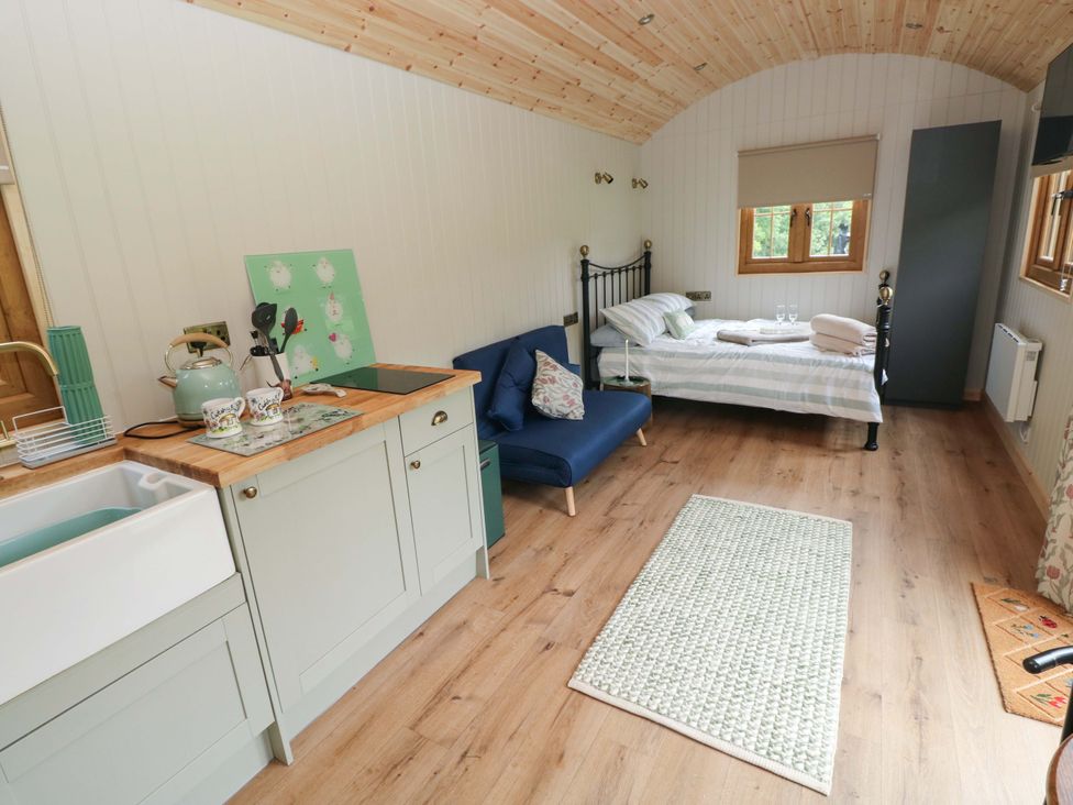 A bedroom with a bed, sofa, and kitchen area at Shepherd Hut 1 in Llandeilo