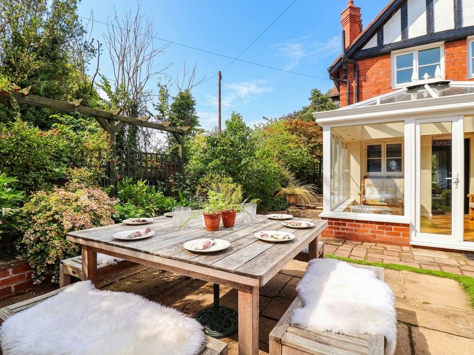 A garden with a wooden table, plates, and flower pots at Lyneal Cottage in Ellesmere