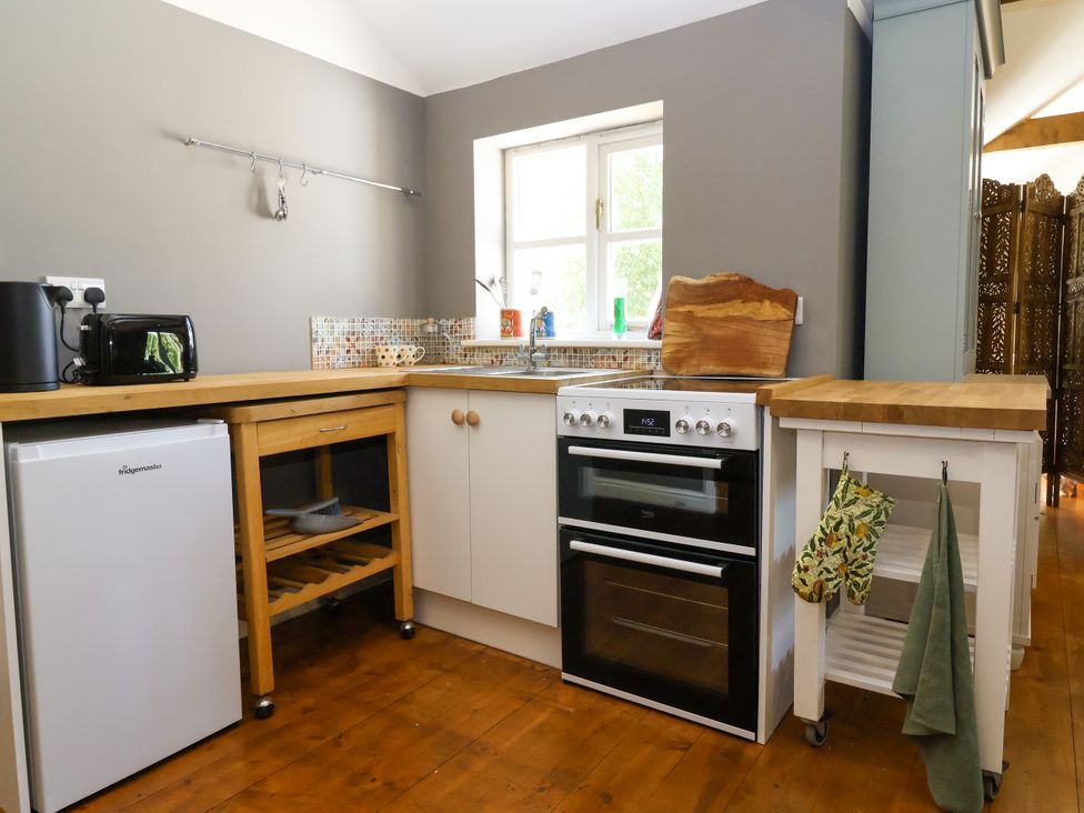 A kitchen with a refrigerator, oven, sink, and storage units at The Old Dairy in Corsley near Warminster