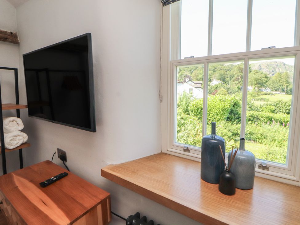 A living room with a television and view of the outdoors at Haws Bank Cottage in Coniston