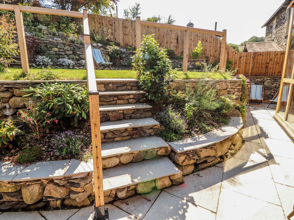 A garden with stone steps leading up to plants and a wooden fence at Haws Bank Cottage in Coniston