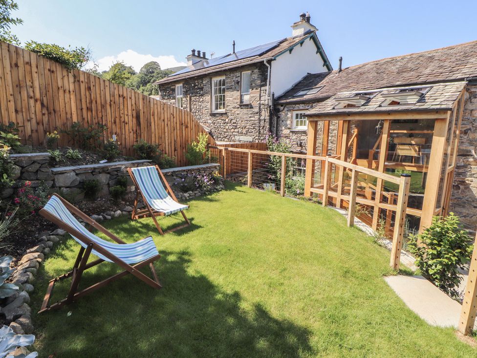 A garden with deck chairs and a wooden fence at Haws Bank Cottage in Coniston