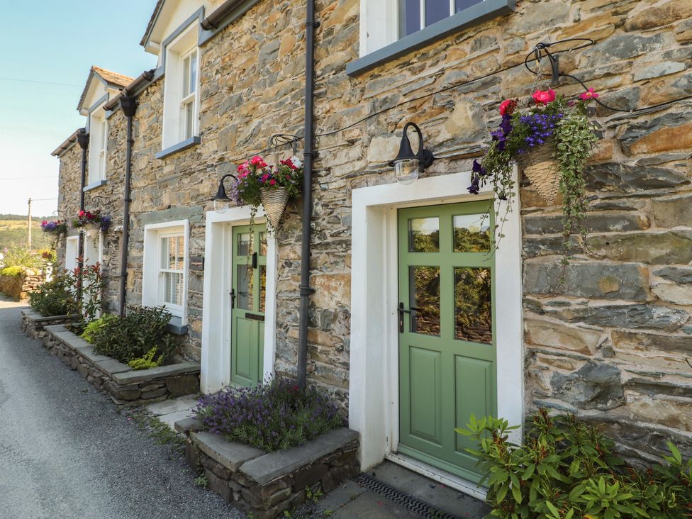 An outdoor view of stone cottages with green doors and hanging flowers at Haws Bank Cottage in Coniston