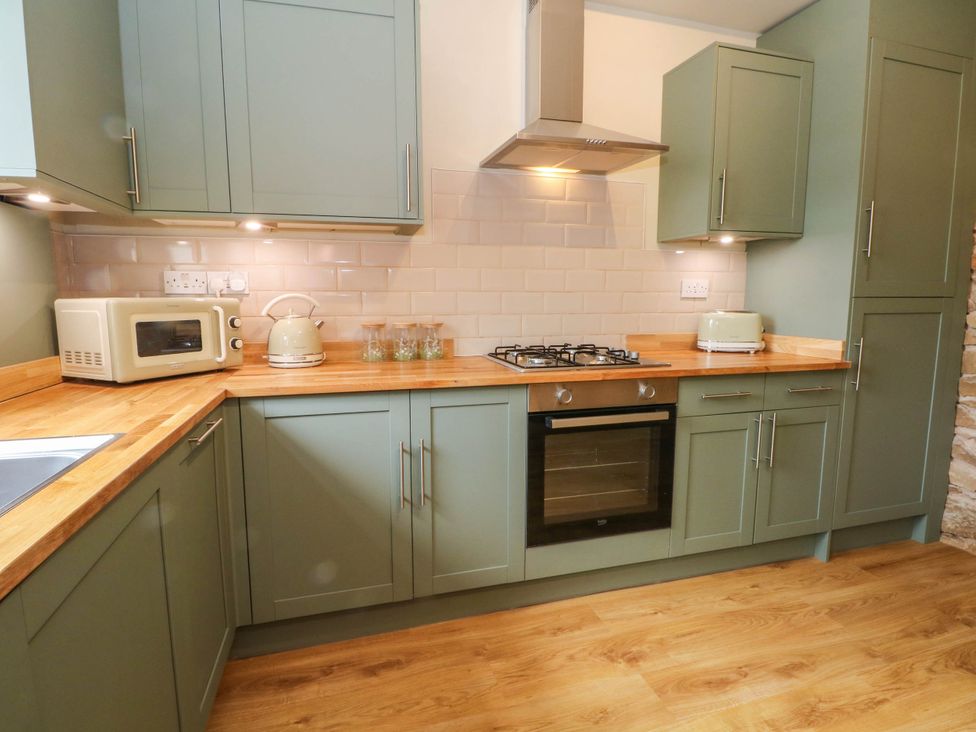 A kitchen with a microwave, kettle, and gas stove at 2 Bentley Bridge Cottages in Matlock