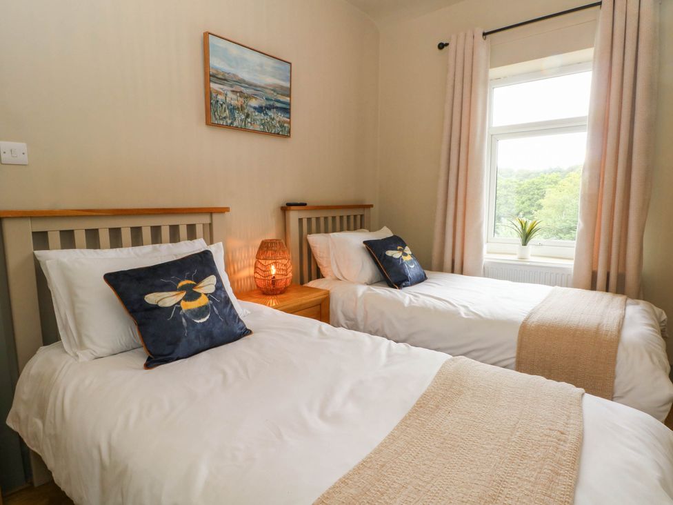 A bedroom with two single beds, a lamp, and a window at 2 Bentley Bridge Cottages in Matlock