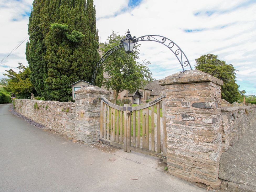 A gate and stone wall with trees at Kwerky Cottage, Lydbury North