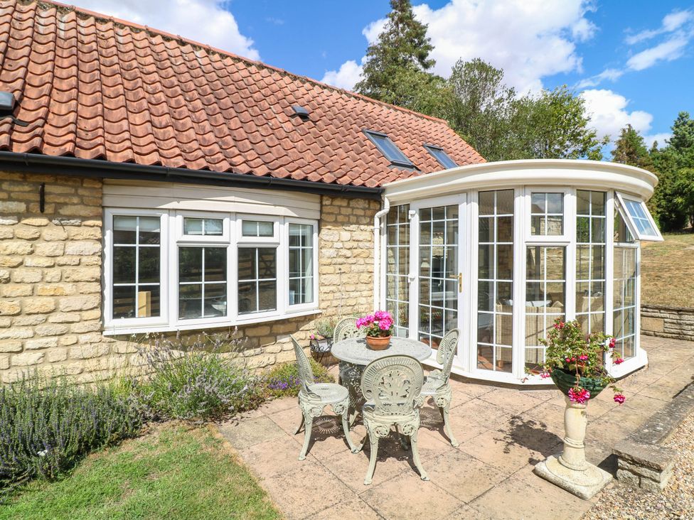 A garden with a conservatory and seating at Wheelwrights Cottage in Corby Glen