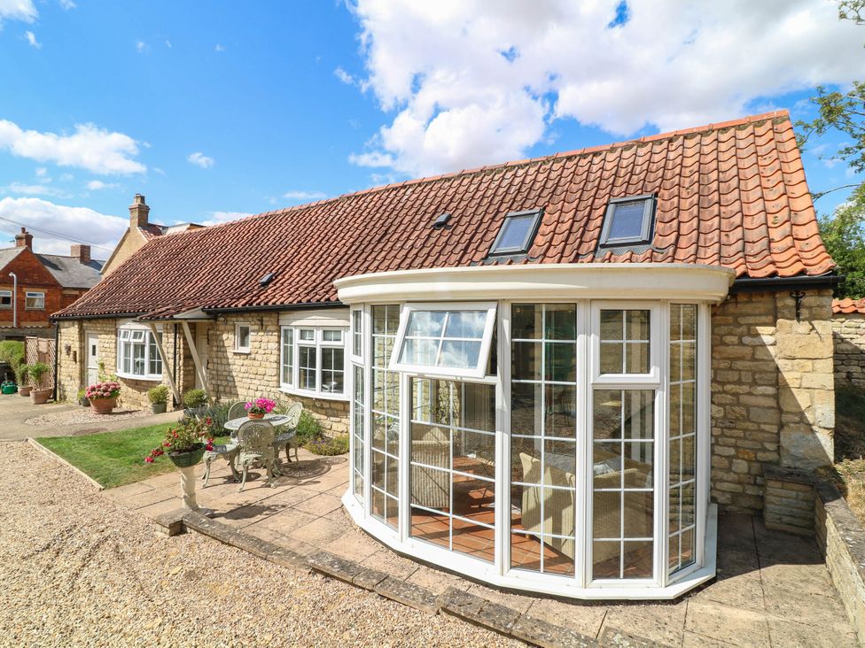 A conservatory with flowers and seating at Wheelwrights Cottage in Corby Glen