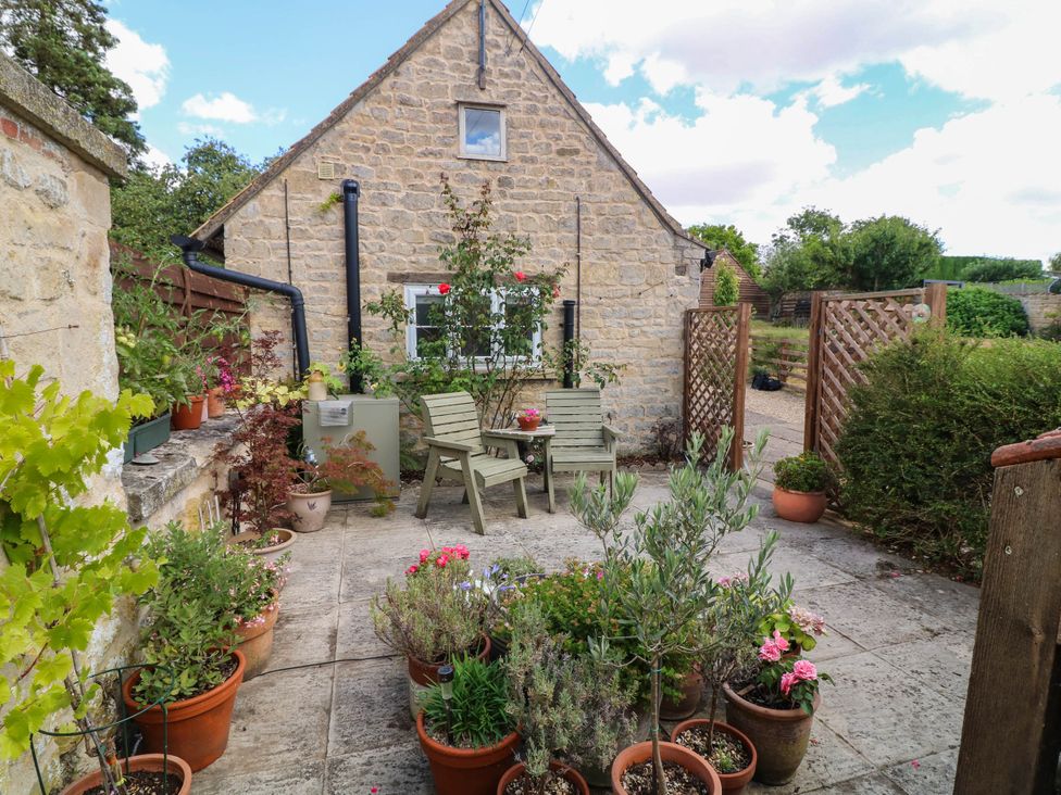 A garden with stone walls, potted plants, and garden furniture at Wheelwrights Cottage in Corby Glen