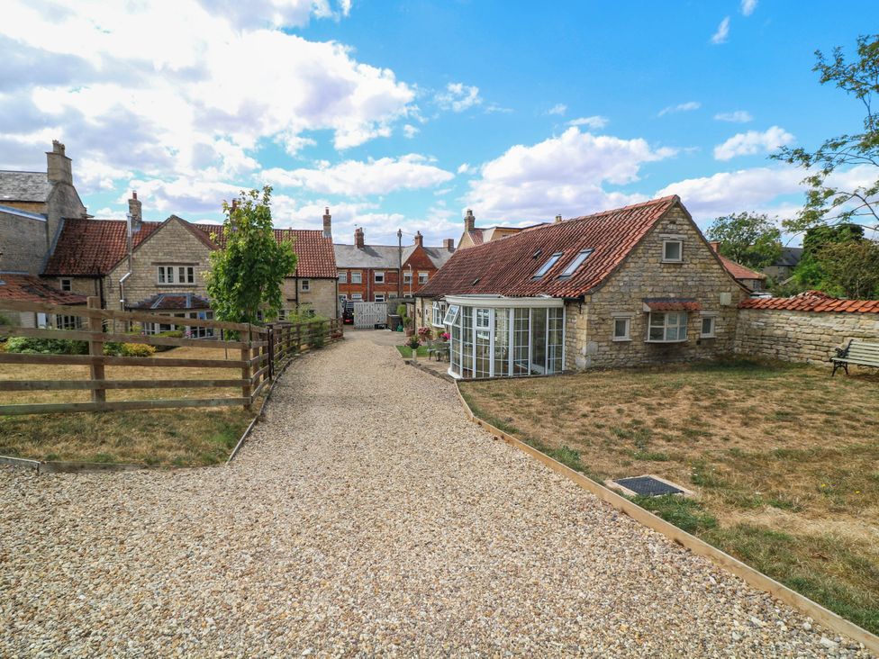 An outdoor view of a cottage with a gravel driveway at Wheelwrights Cottage in Corby Glen