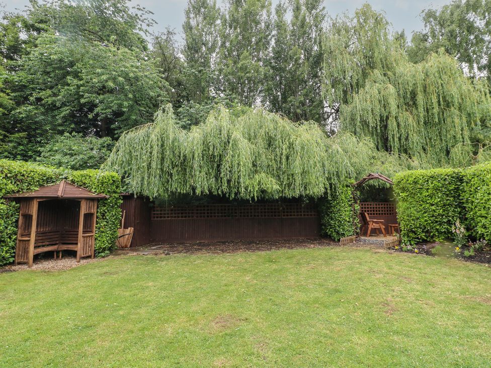 A garden with a willow tree and two wooden gazebos at The Kingfisher Falls in Melton Mowbray