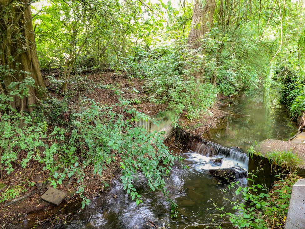 Water flowing through a stream surrounded by trees and bushes at The Kingfisher Falls in Melton Mowbray