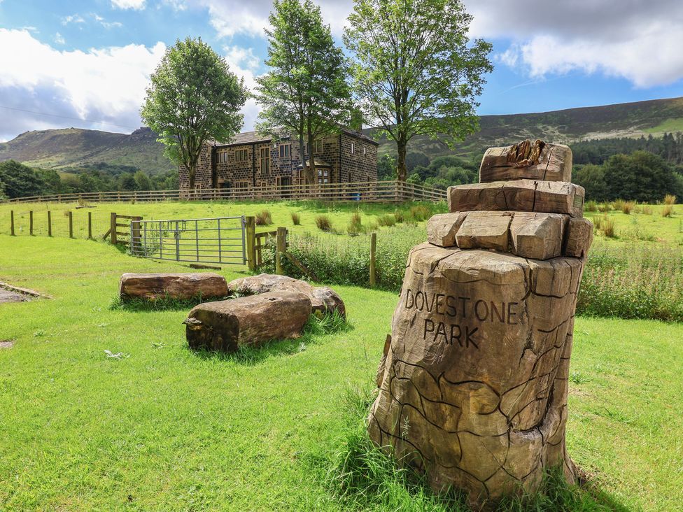 A grassy area with a wooden building and trees at Dovestone Park near Greenfield