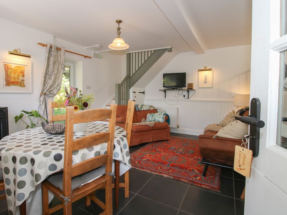 A living room with a dining table, couch, and television at Chess Cottage in Weobley