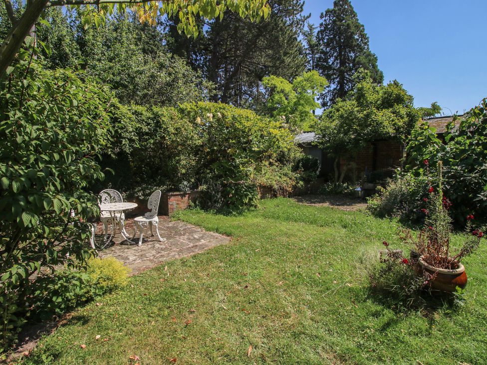 A garden with a table and chair on paving stones at Chess Cottage in Weobley